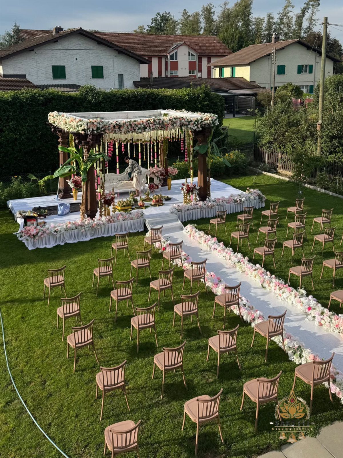 Outdoor wedding ceremony venue with a floral mandap and white aisle on grass.