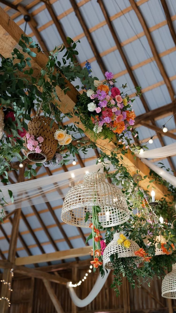 Rustic barn ceiling decorated with colorful flowers, greenery, and woven wicker lanterns.
