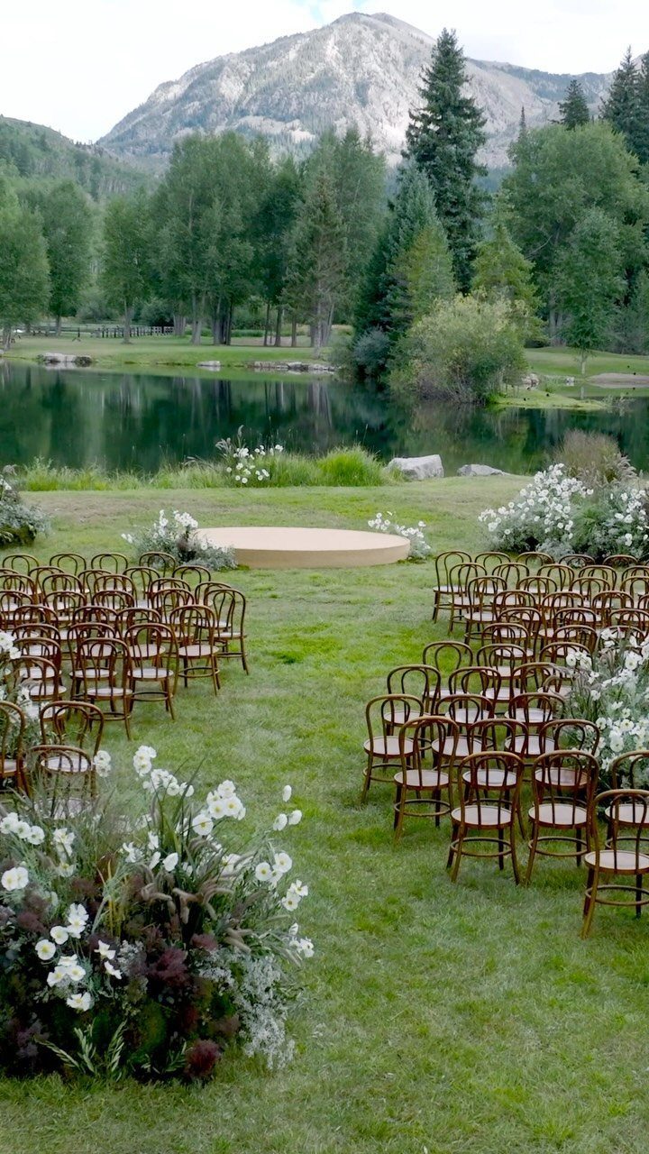 Outdoor wedding ceremony setup with wooden chairs and a circular platform by a lake.