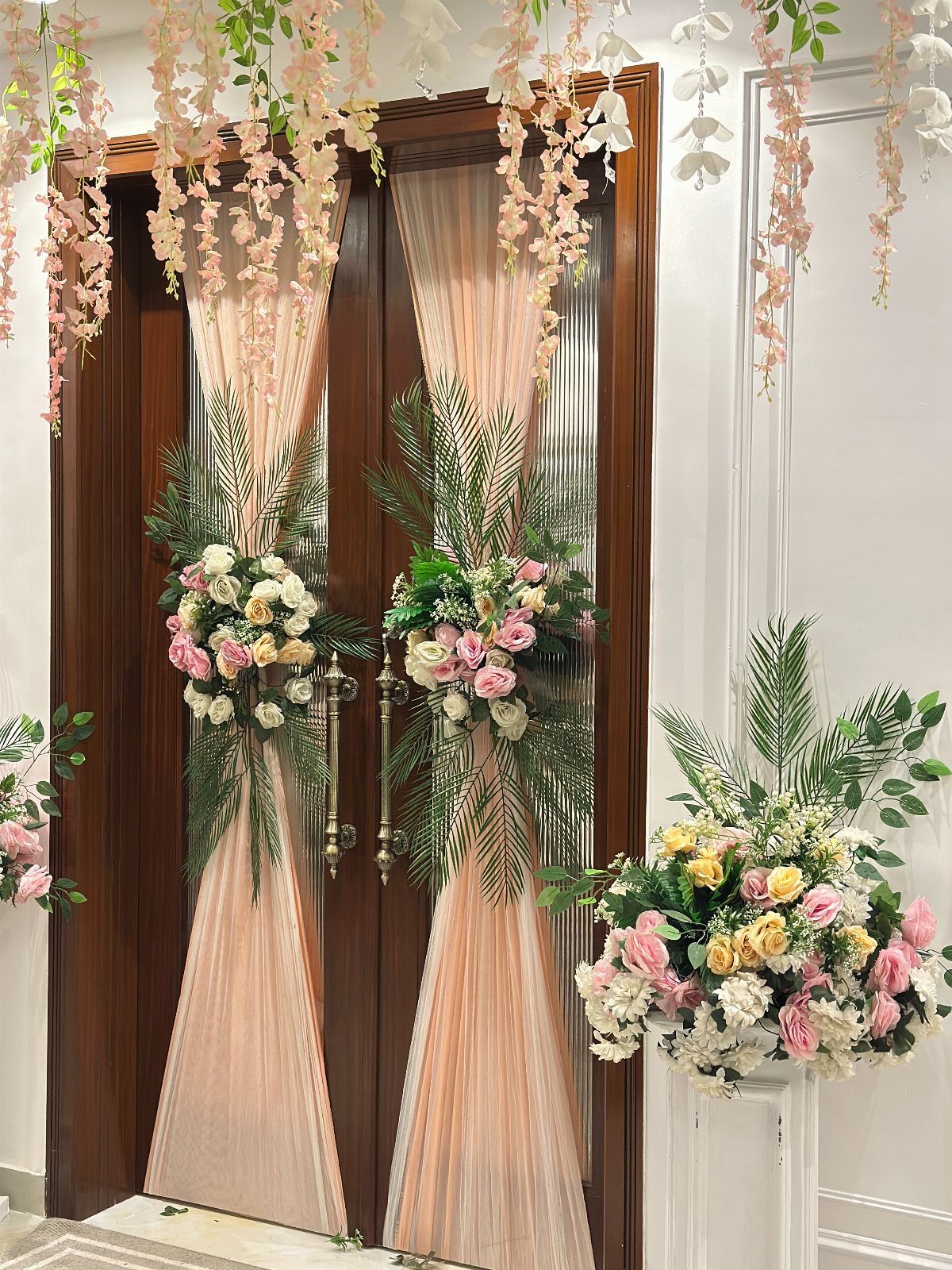 19 Wedding Decorations at Home: DIY Ideas to Try 17 Floral arrangements and peach fabric decorating wooden doors with hanging flowers above.