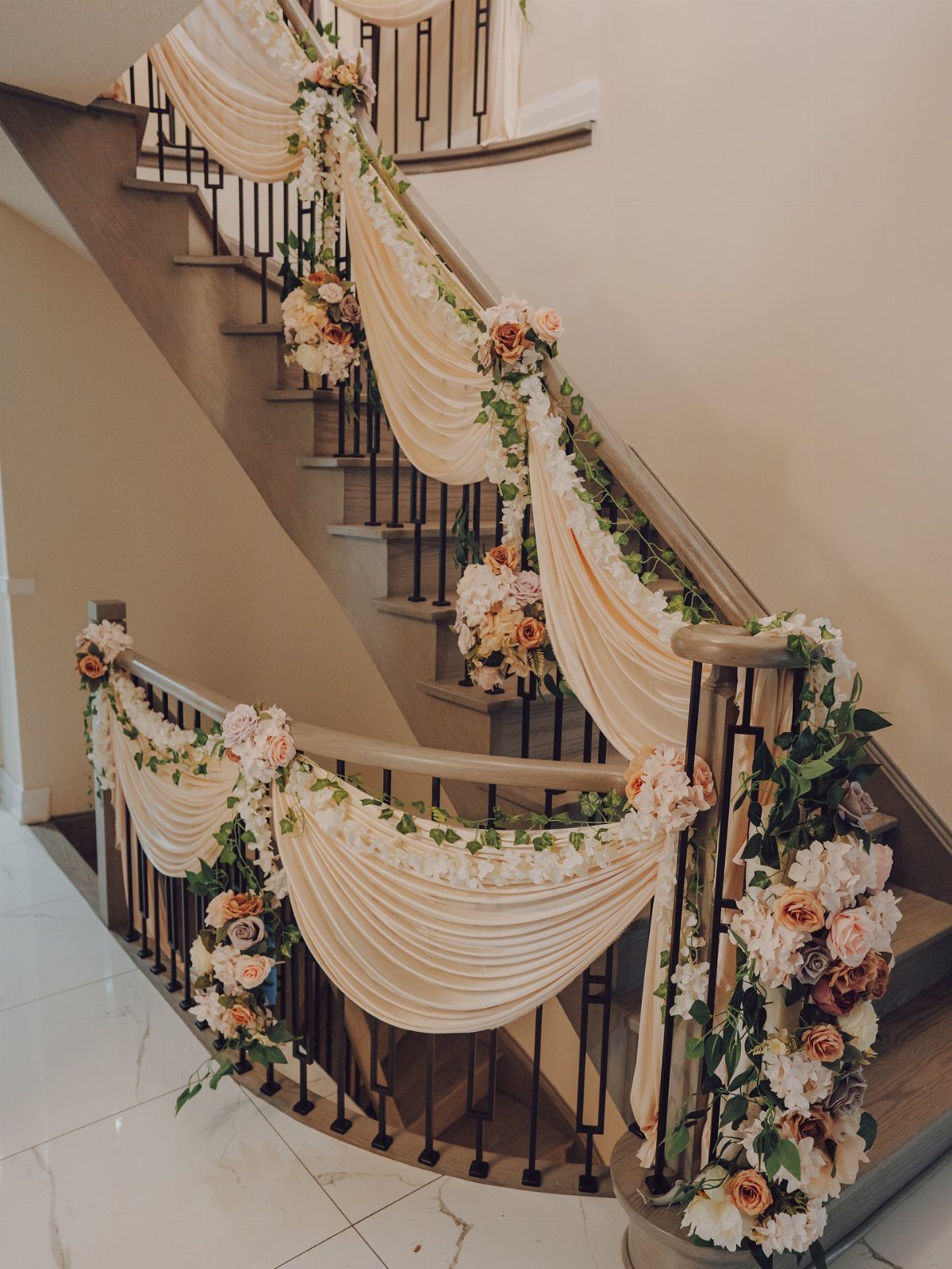 19 Wedding Decorations at Home: DIY Ideas to Try 16 Cream fabric swags and peach roses decorating a curved indoor staircase railing.