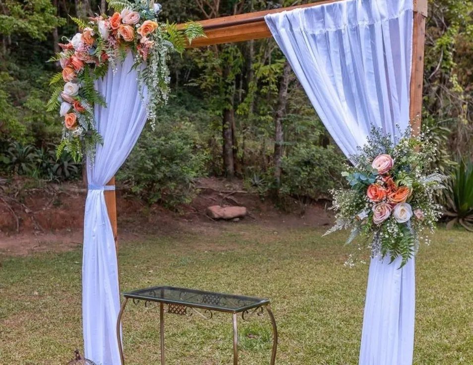 19 Wedding Decorations at Home: DIY Ideas to Try 7 Wooden wedding ceremony arch with white fabric and peach floral arrangements on grass