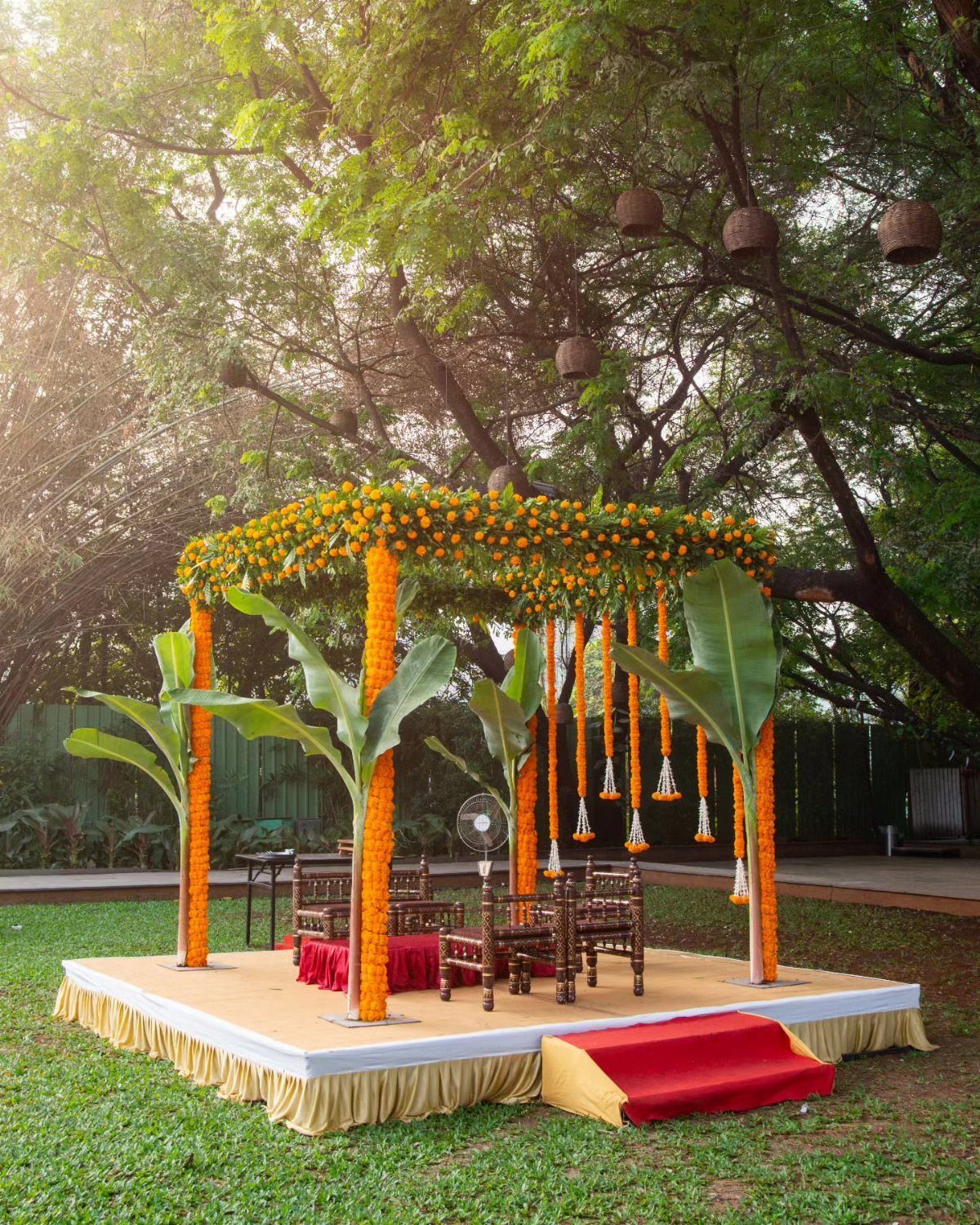 19 Wedding Decorations at Home: DIY Ideas to Try 19 Wedding mandap with orange marigold garlands and banana leaves under leafy trees.