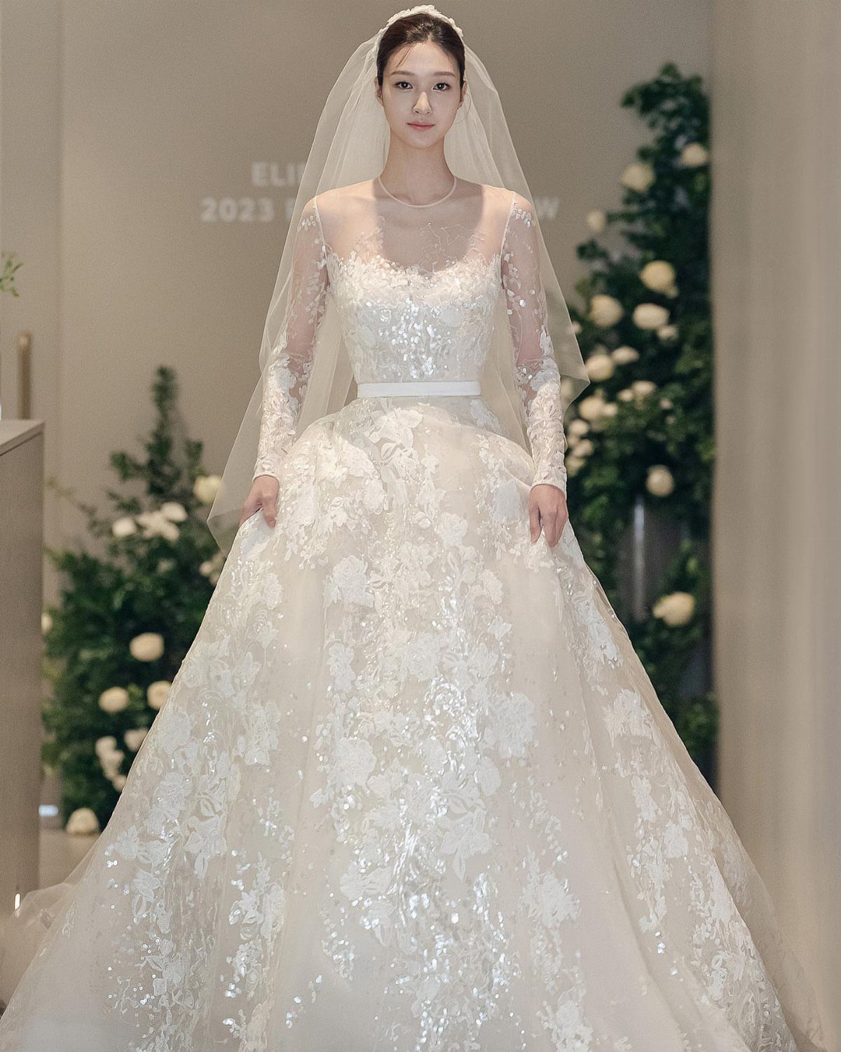 Woman in an intricate white lace wedding gown with a long sheer veil.