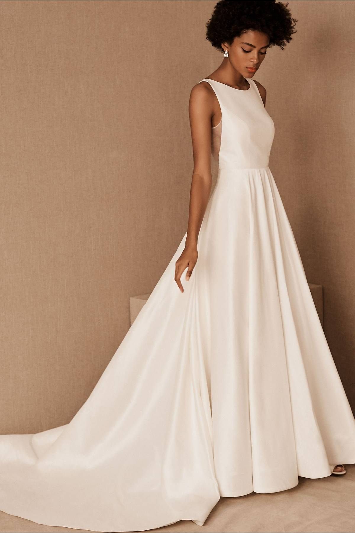 Woman wearing a minimalist white satin wedding gown with a full flowing skirt.