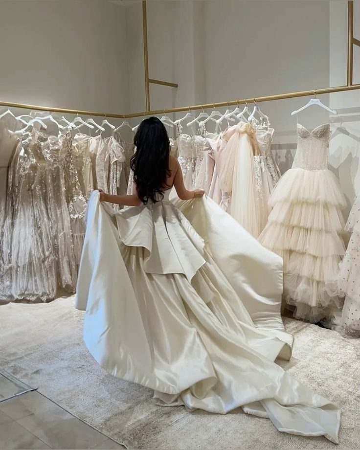 Woman wearing a voluminous white satin wedding gown with a large bow in boutique.