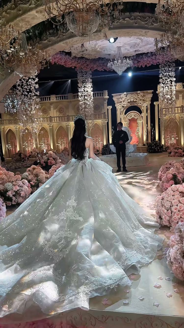 Woman in a sparkling white wedding gown with a long dramatic train in a ballroom.
