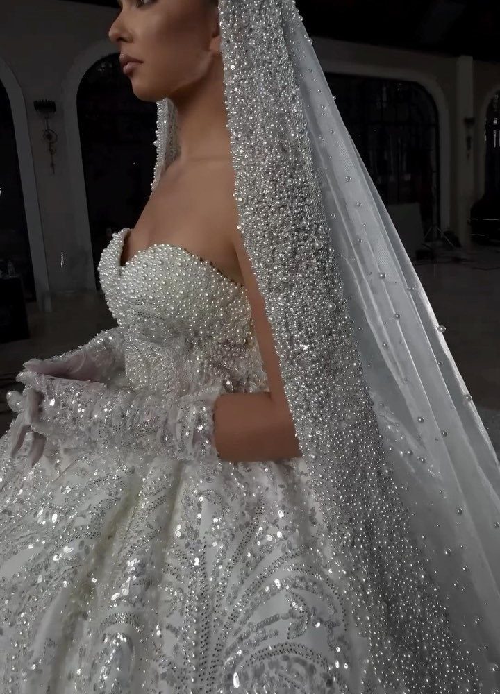 Woman in a white strapless wedding gown with heavy sequins and a sparkling veil.