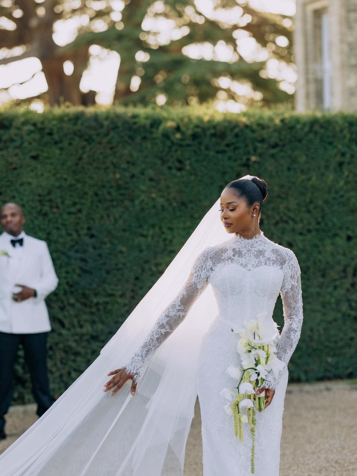 Woman in a white lace wedding dress with a long veil and lily bouquet.