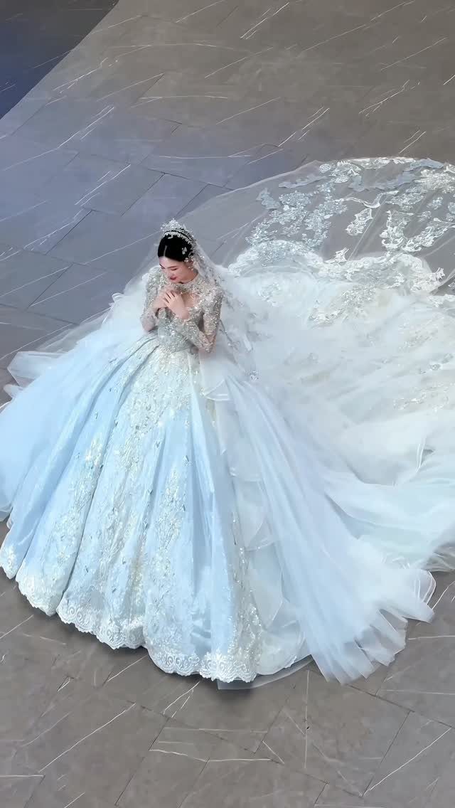 Woman in a voluminous light blue ball gown wedding dress with a long lace train.