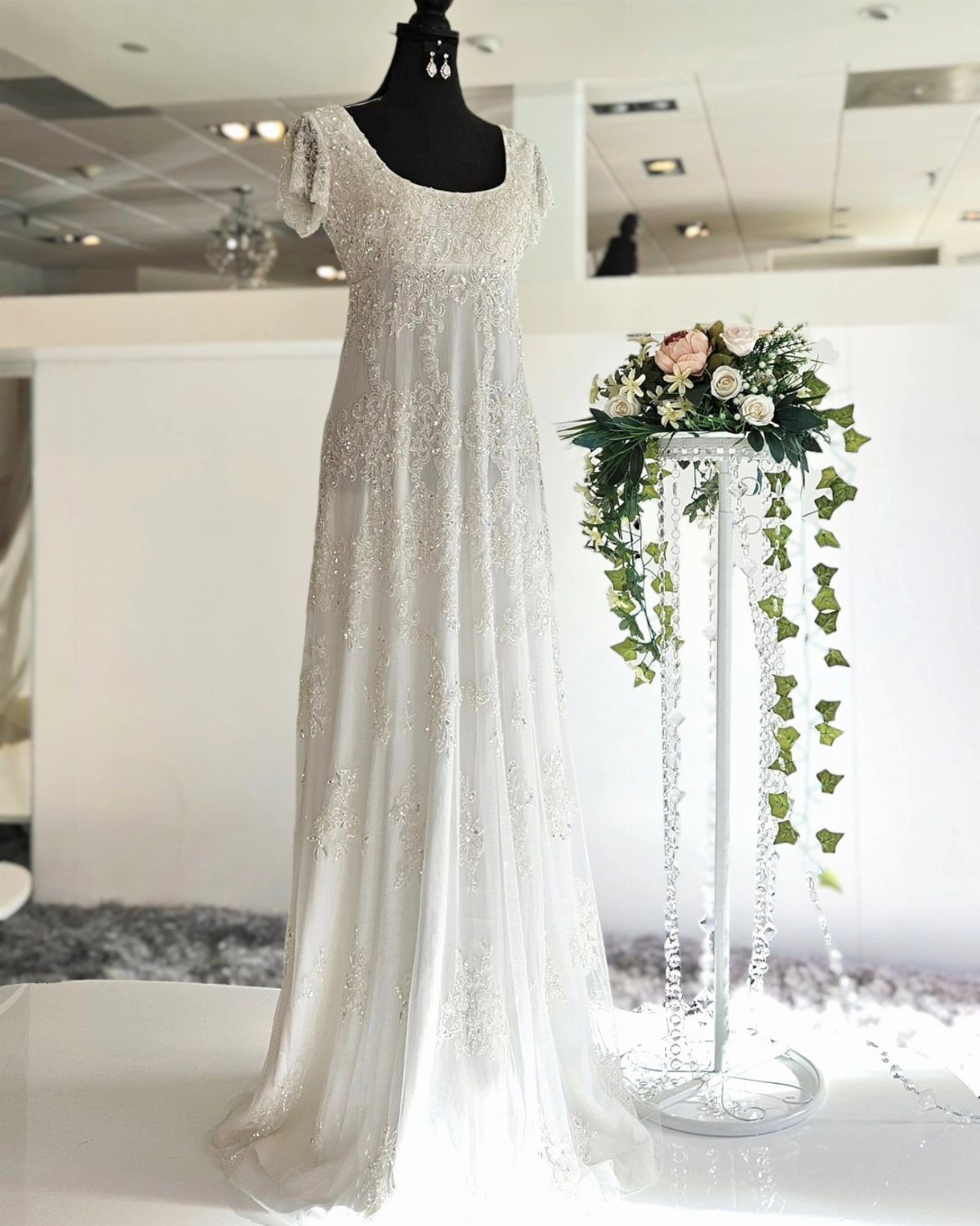 White empire waist wedding dress with silver embroidery on a black mannequin.
