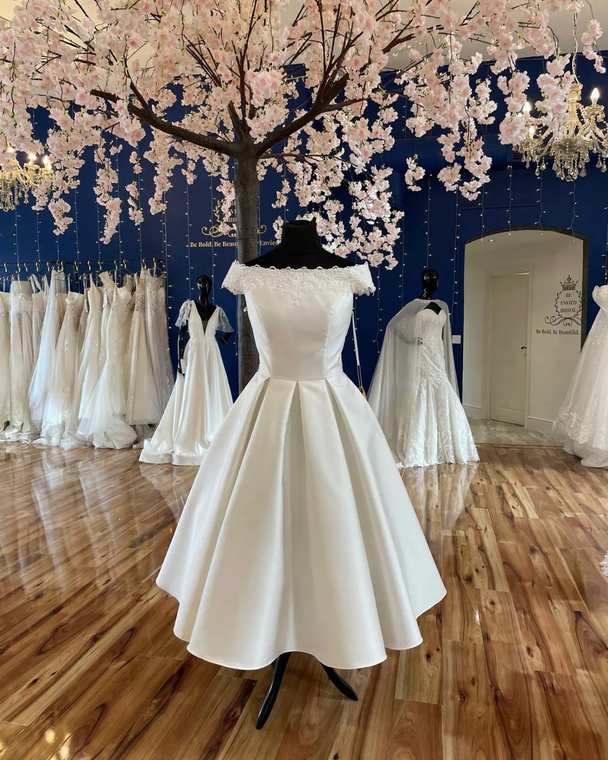 White off-the-shoulder tea-length wedding dress on a mannequin in a bridal boutique.