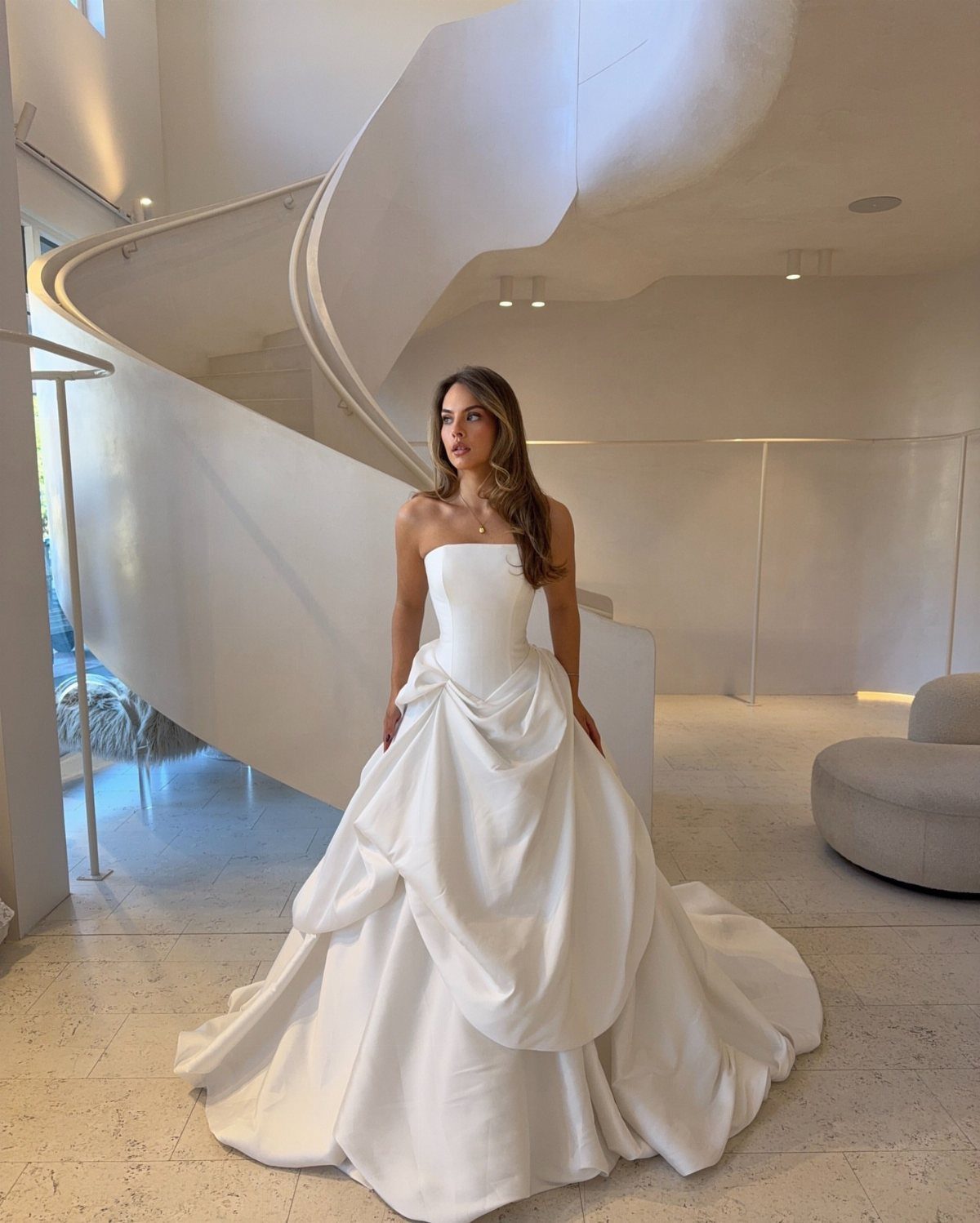 Wedding Dresses Elegant and Classy: 14 Gown Styles 10 Woman in a voluminous white satin strapless wedding gown standing by a spiral staircase.