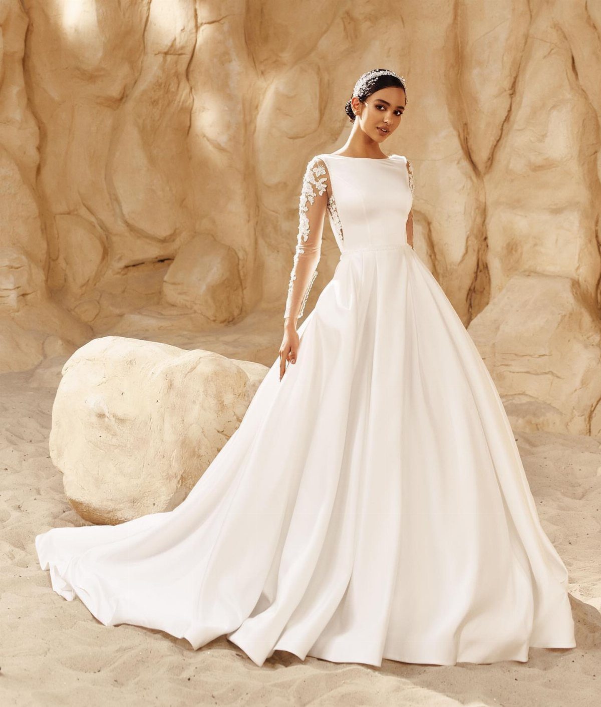 Wedding Dresses Elegant and Classy: 14 Gown Styles 14 Woman in a white satin wedding dress with lace sleeves against sandy rocks.