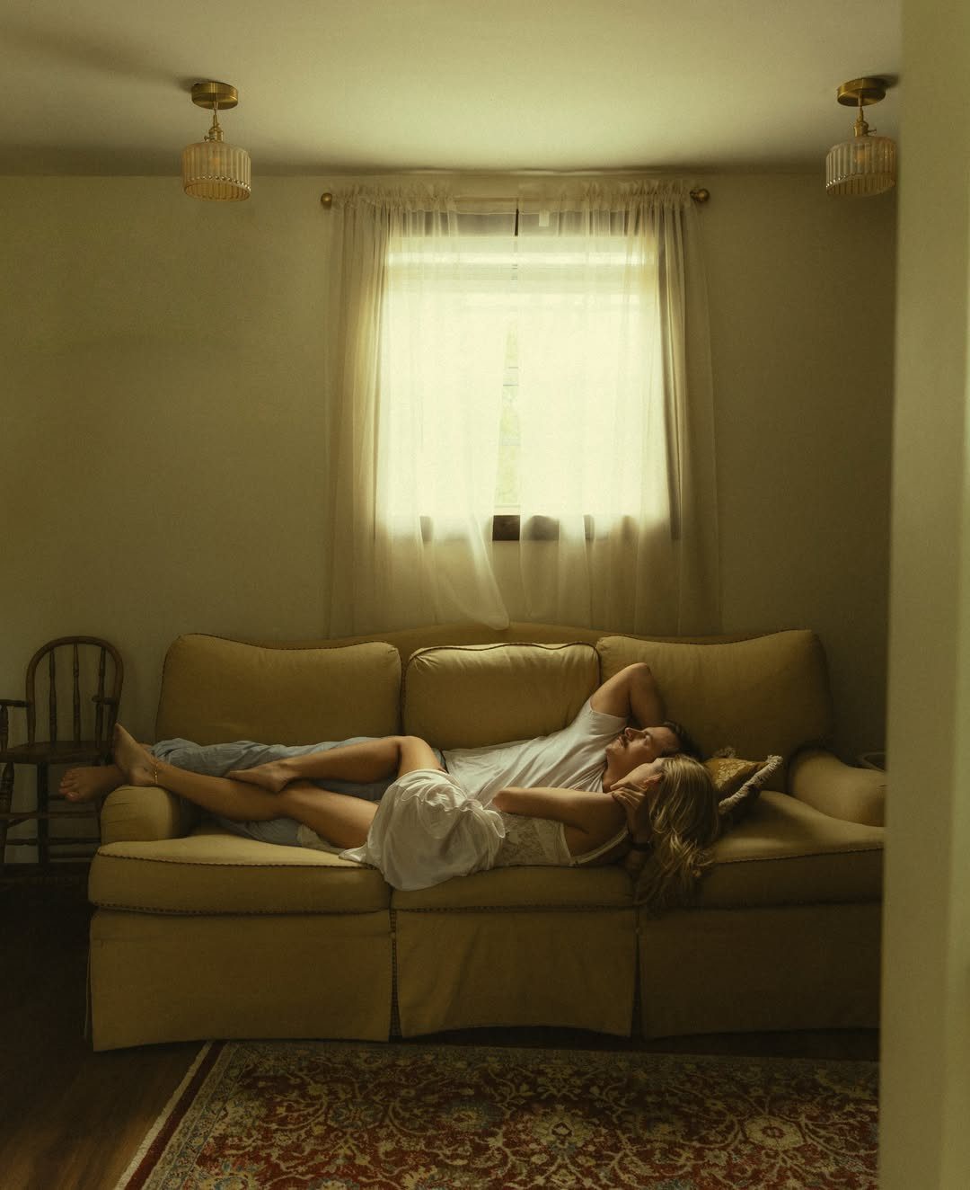 Couple cuddling on a tan sofa in a room with soft window light.