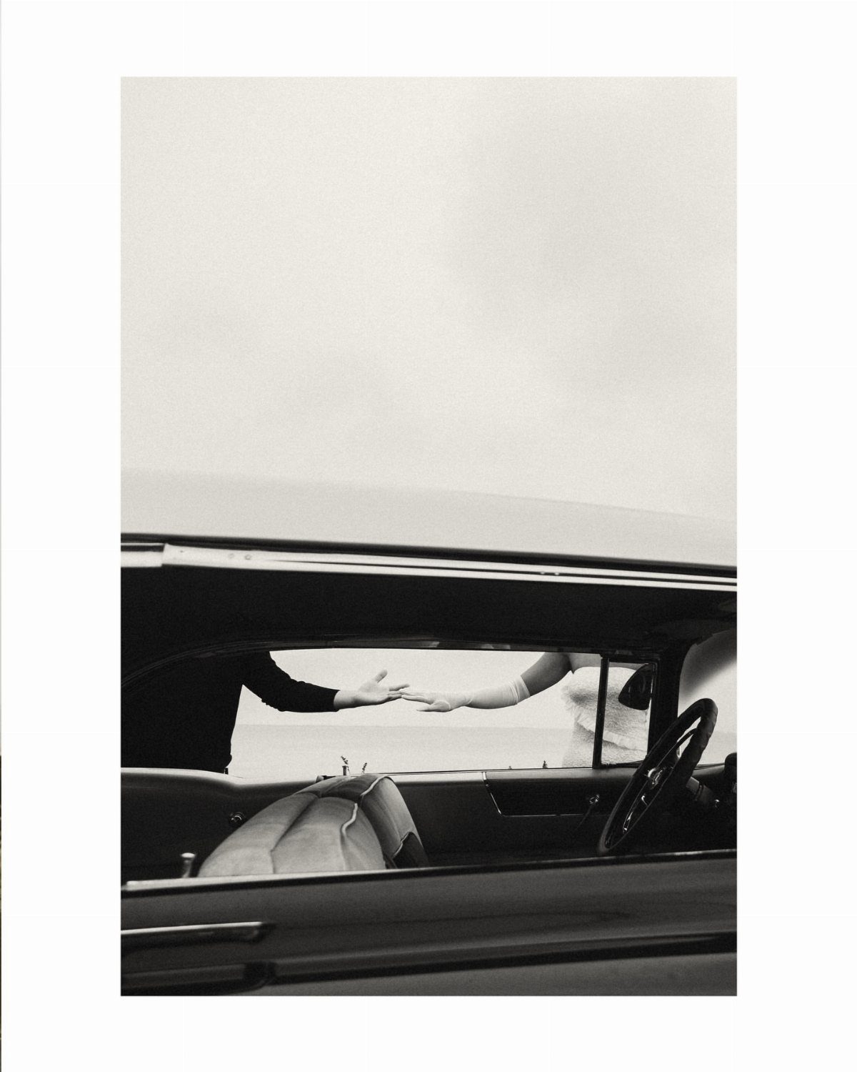 Two people reaching for each other's hands through a vintage car window.