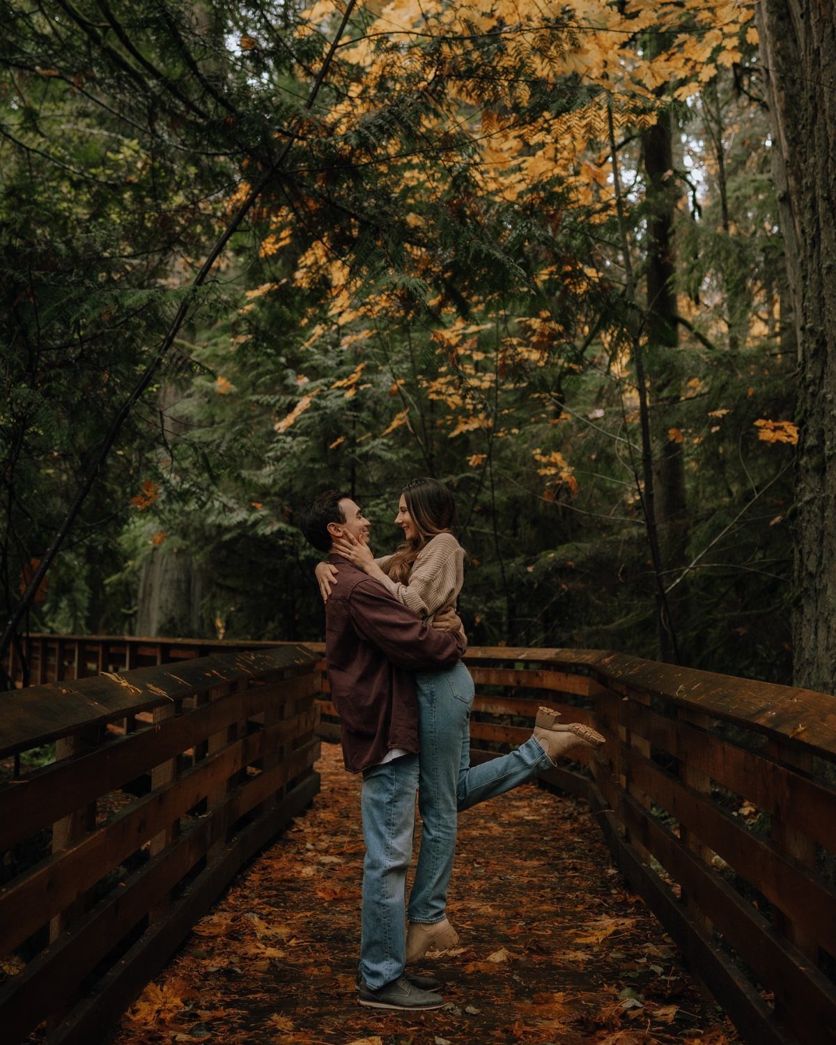 Couple embracing on a wooden bridge surrounded by autumn forest foliage