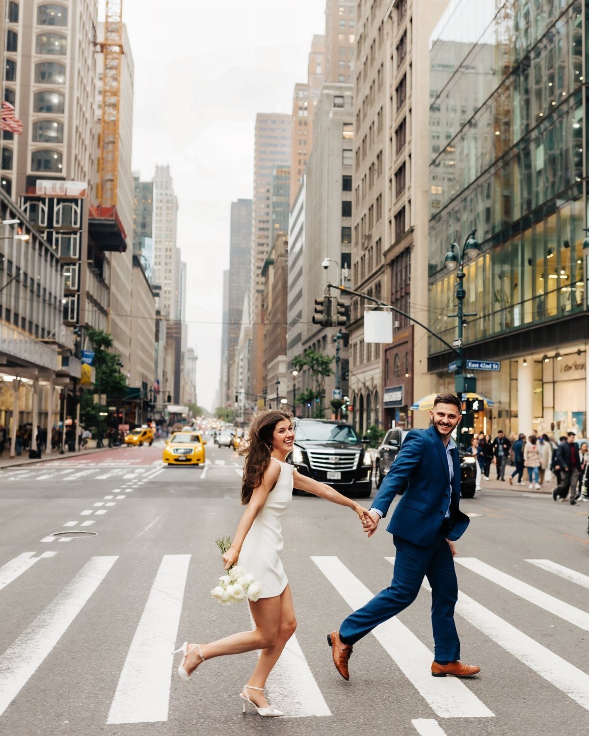 Couple holding hands and smiling while crossing a street between Manhattan skyscrapers
