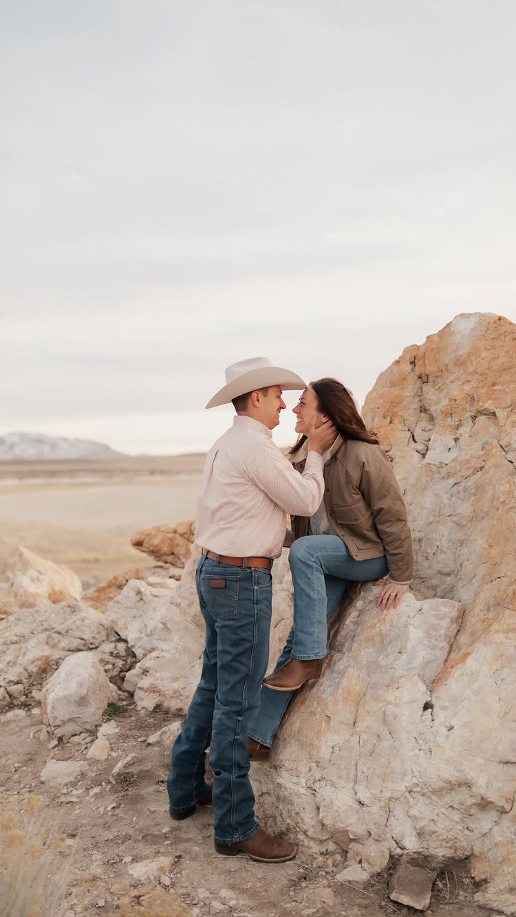 Couple in western attire gazing at each other against a rocky desert backdrop.