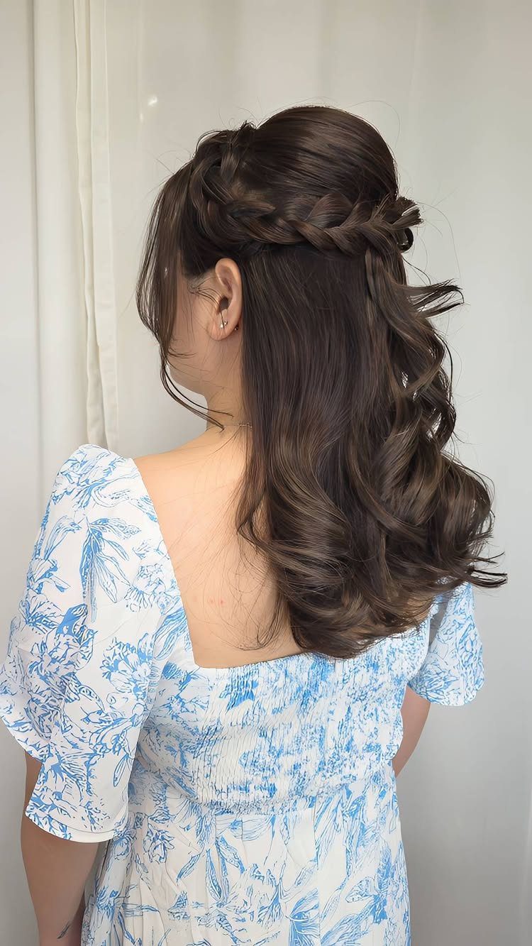 Woman with brown hair styled in a braided half-up look with loose curls.