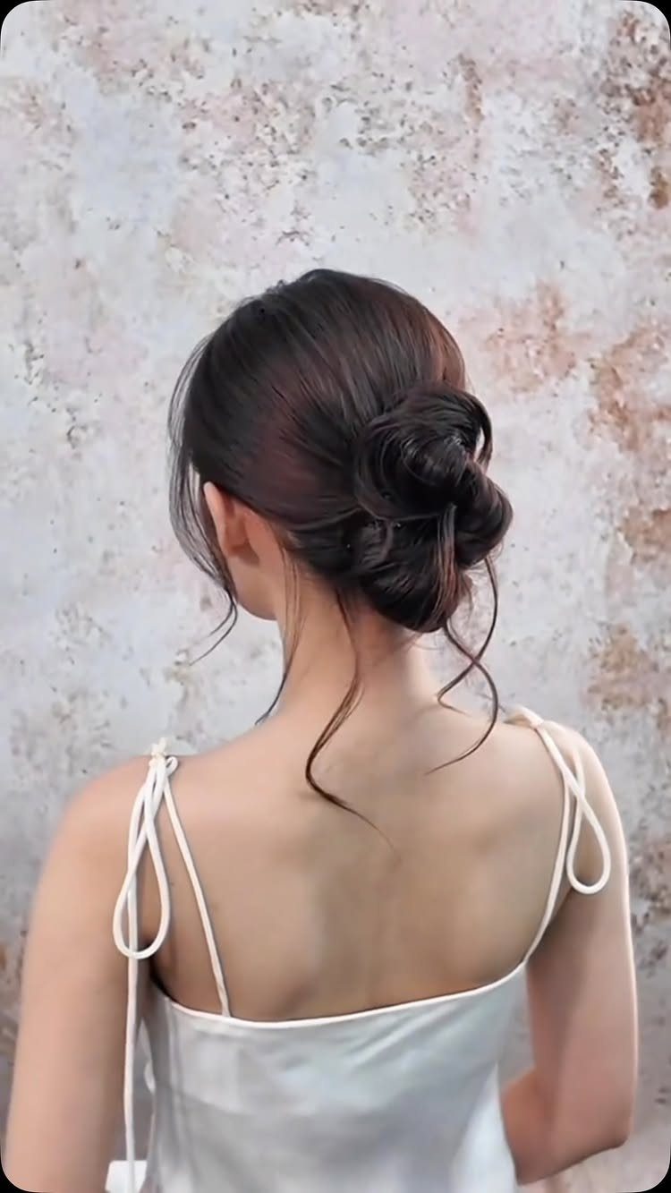 Dark brown hair styled in a classic low chignon bun with loose strands.