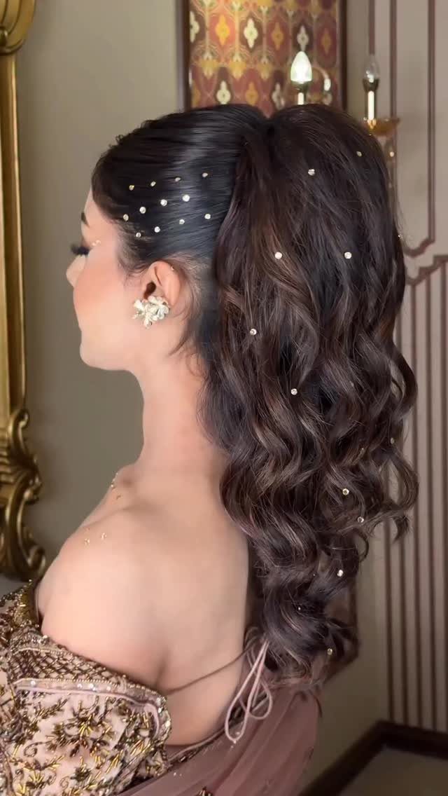 Woman with a voluminous curly ponytail adorned with small white pearls and floral earring.