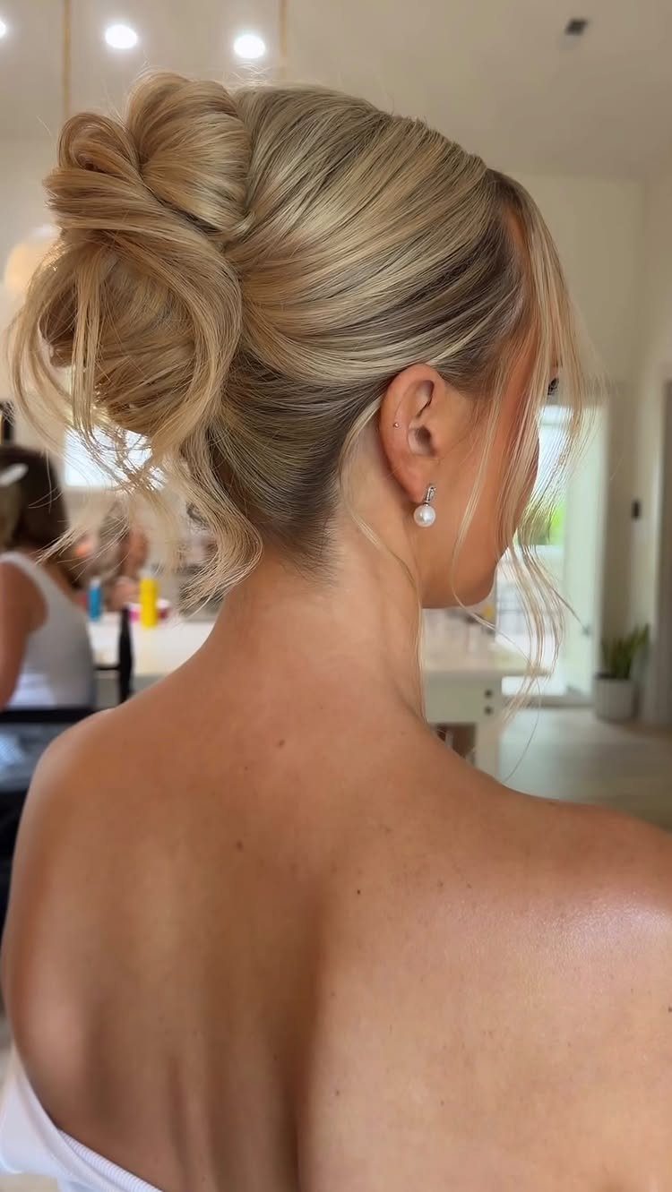 Blonde woman with a voluminous textured high bun and a pearl earring.
