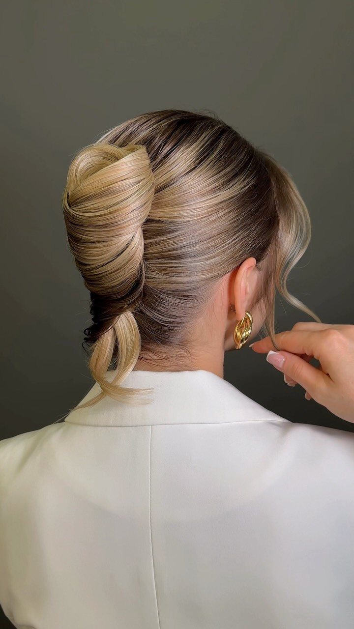 Blonde highlighted hair styled in a polished sculpted updo with a white blazer.