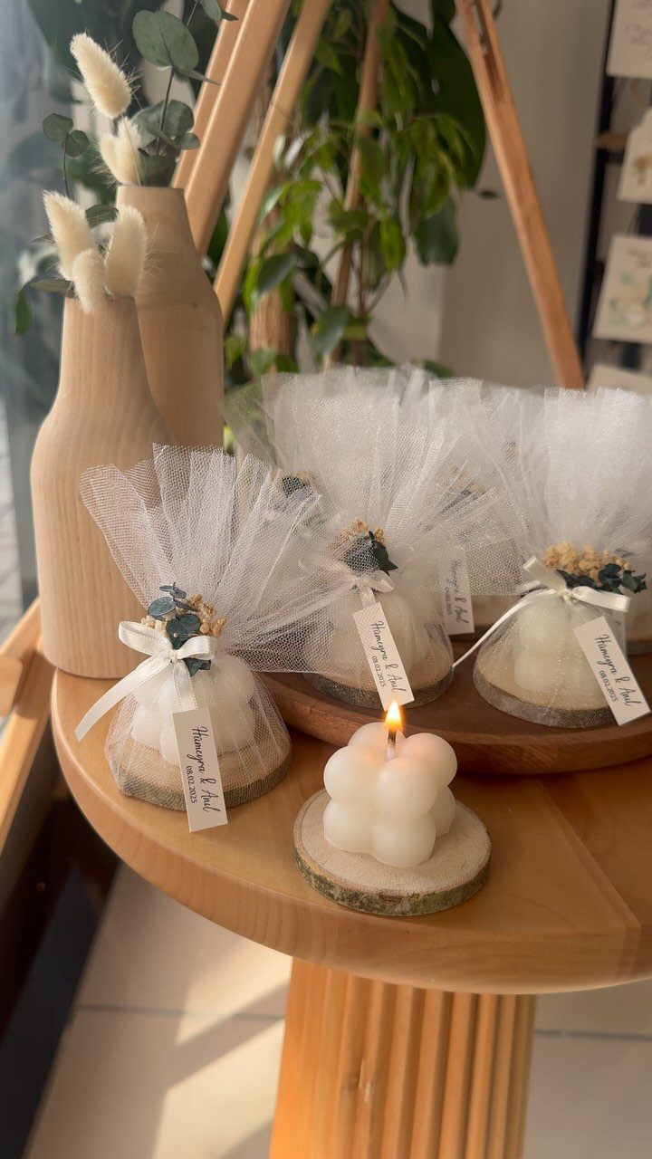 30 Wedding Guest Keepsakes Your Guests Will Actually Use 2 White bubble candles on wooden slices wrapped in tulle with ribbons and tags.