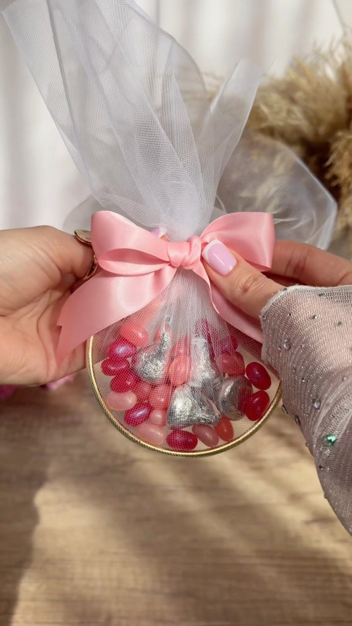 30 Wedding Guest Keepsakes Your Guests Will Actually Use 18 White tulle gift bag with pink bow filled with heart-shaped candies.