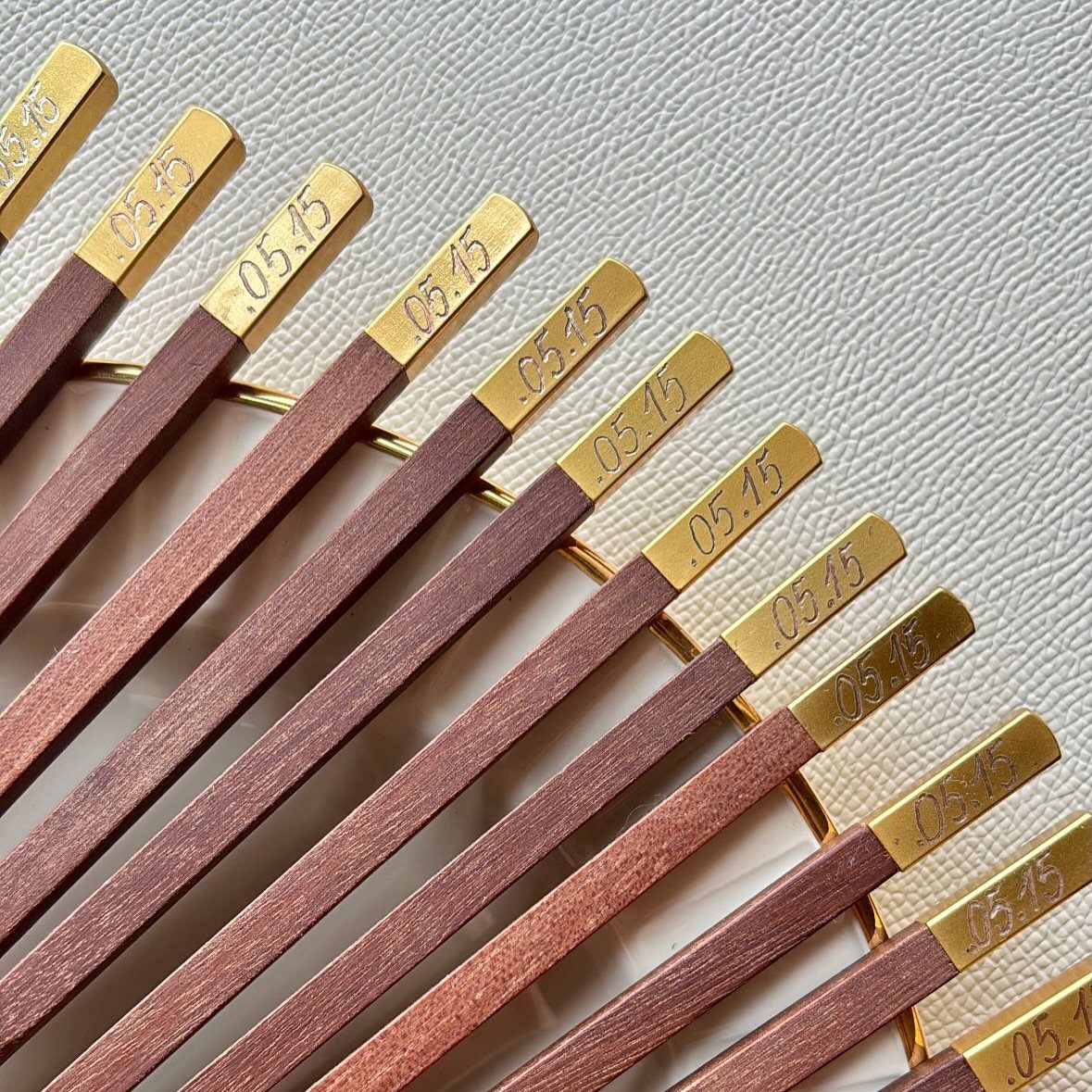 30 Wedding Guest Keepsakes Your Guests Will Actually Use 11 Wooden chopsticks with gold tips engraved with the date .05.15 on a white background.