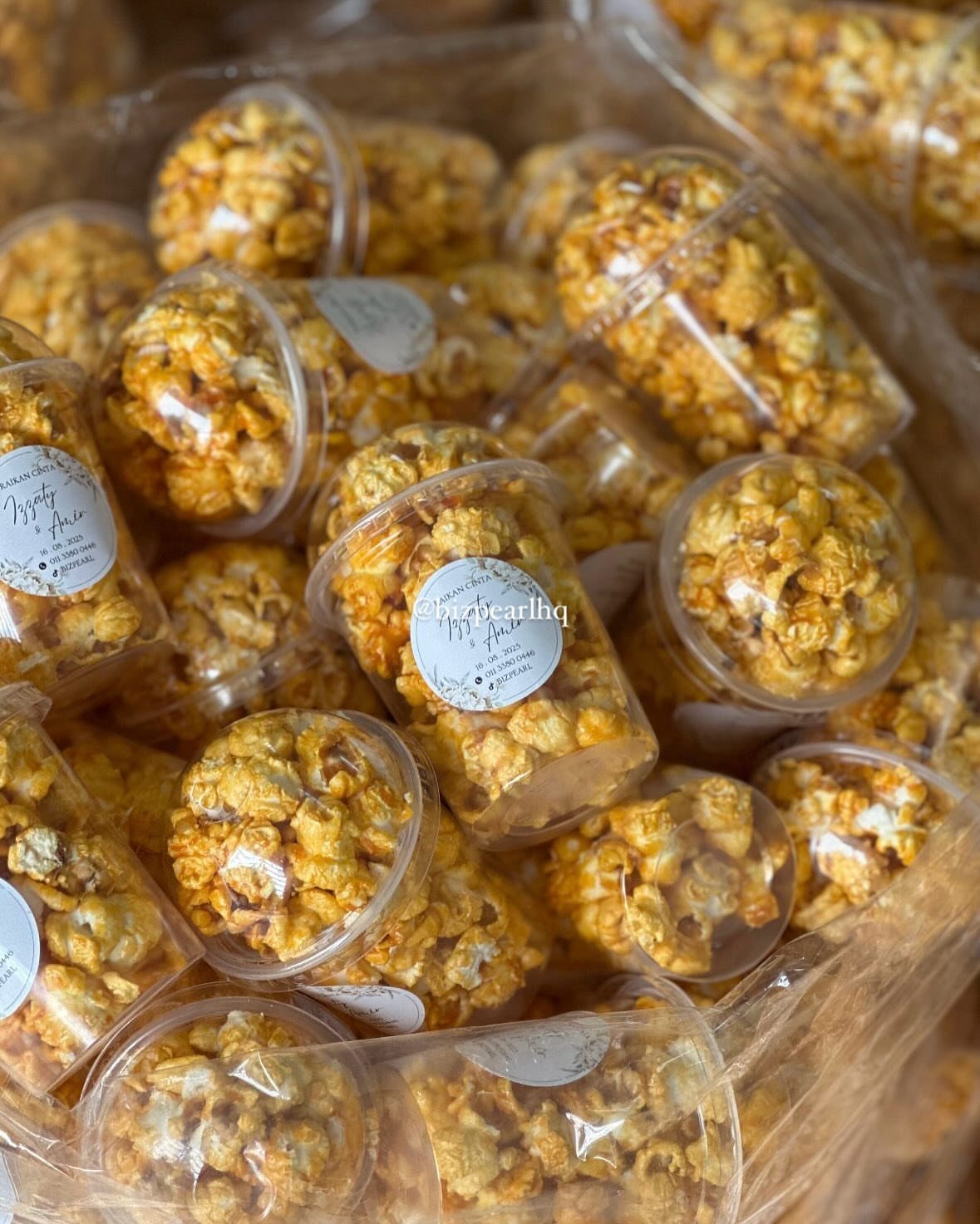 30 Wedding Guest Keepsakes Your Guests Will Actually Use 25 Caramel popcorn in small clear plastic containers with white circular labels.