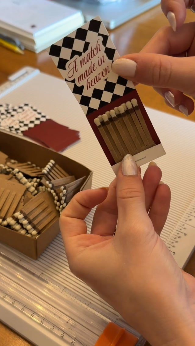 30 Wedding Guest Keepsakes Your Guests Will Actually Use 26 Custom wedding matchbox with checkered border and red text held by hands.