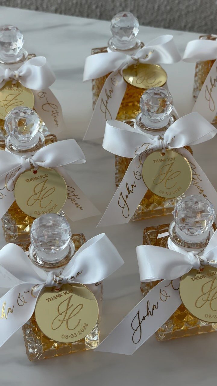 30 Wedding Guest Keepsakes Your Guests Will Actually Use 13 Small glass perfume bottles with white bows and gold circular thank you tags.