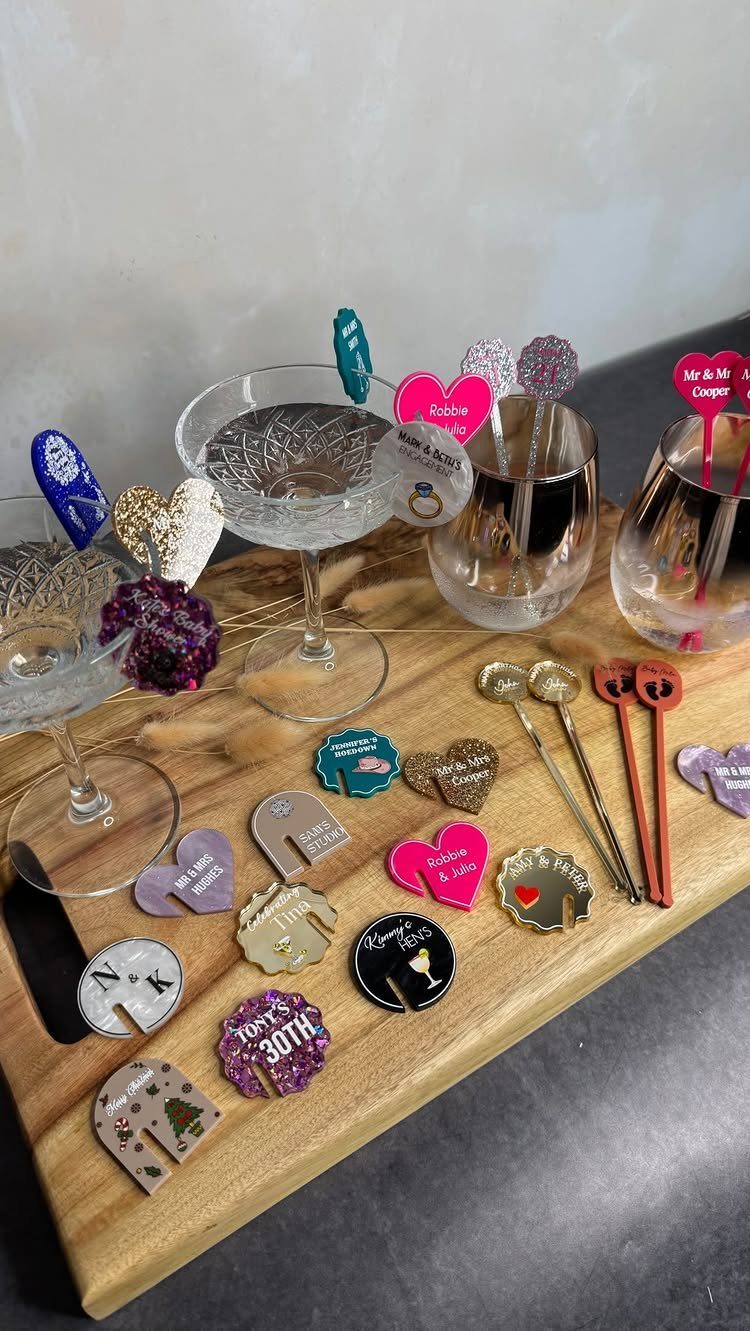 30 Wedding Guest Keepsakes Your Guests Will Actually Use 16 Colorful personalized drink charms and markers displayed on a wooden board with glassware.