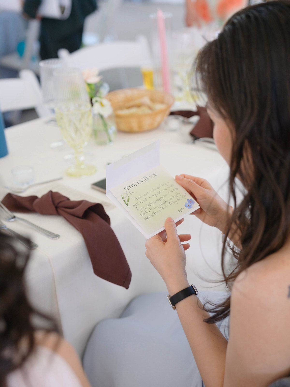 30 Wedding Guest Keepsakes Your Guests Will Actually Use 7 Woman reading a personalized handwritten note at a white wedding reception table.
