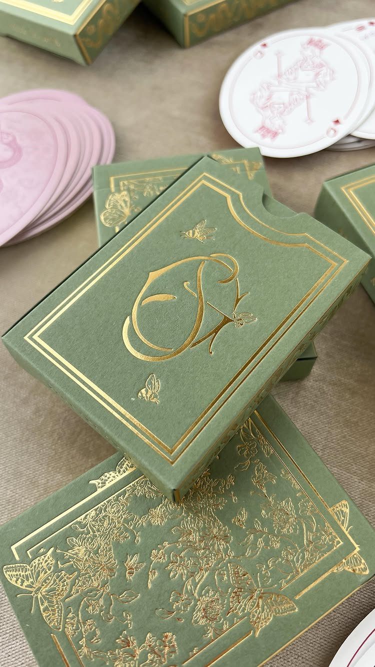 30 Wedding Guest Keepsakes Your Guests Will Actually Use 5 Green gold-embossed playing card boxes and stacks of pink and white cards.
