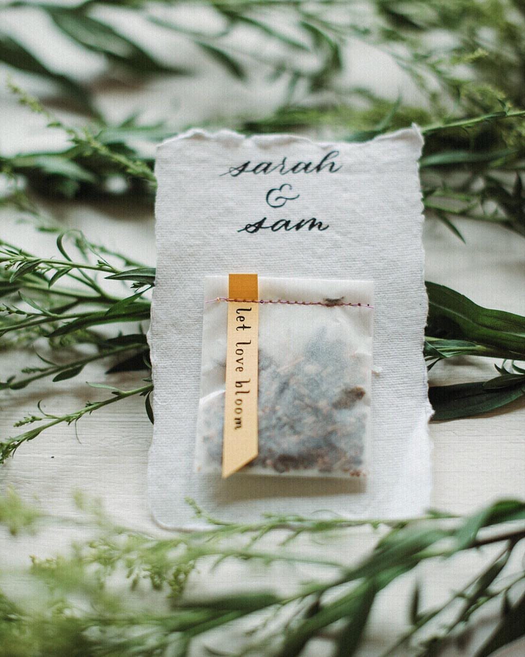 30 Wedding Guest Keepsakes Your Guests Will Actually Use 9 Seed packet with 'let love bloom' label on a personalized wedding napkin.