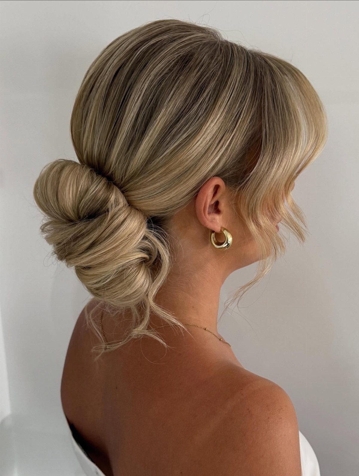 Wedding Hair and Makeup Ideas: 8 Looks for Every Bride 8 Blonde woman with a low textured bridal bun and gold hoop earrings.
