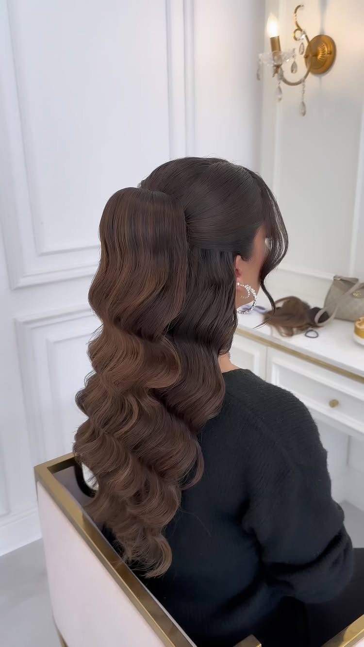 Wedding Hair and Makeup Ideas: 8 Looks for Every Bride 6 Woman with voluminous brown curls in a high ponytail sitting at a vanity.