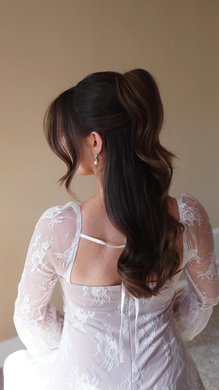 Woman in white lace wedding dress with a high voluminous wavy ponytail hairstyle.