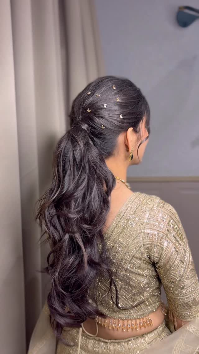 Woman with dark wavy hair in a low ponytail adorned with gold pins.