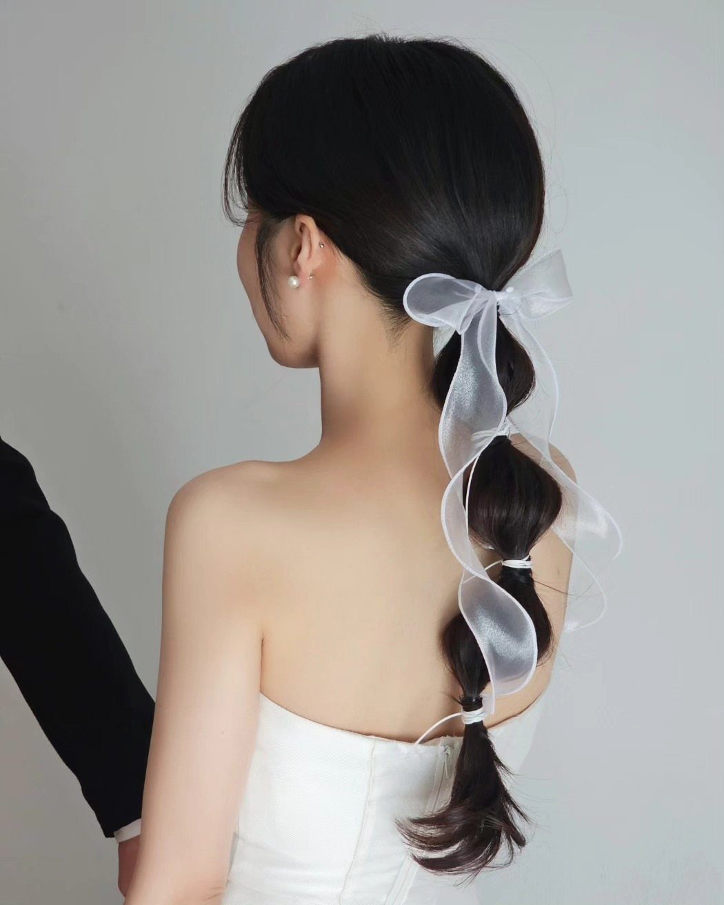 Woman with dark hair in a ponytail featuring a sheer white ribbon bow.