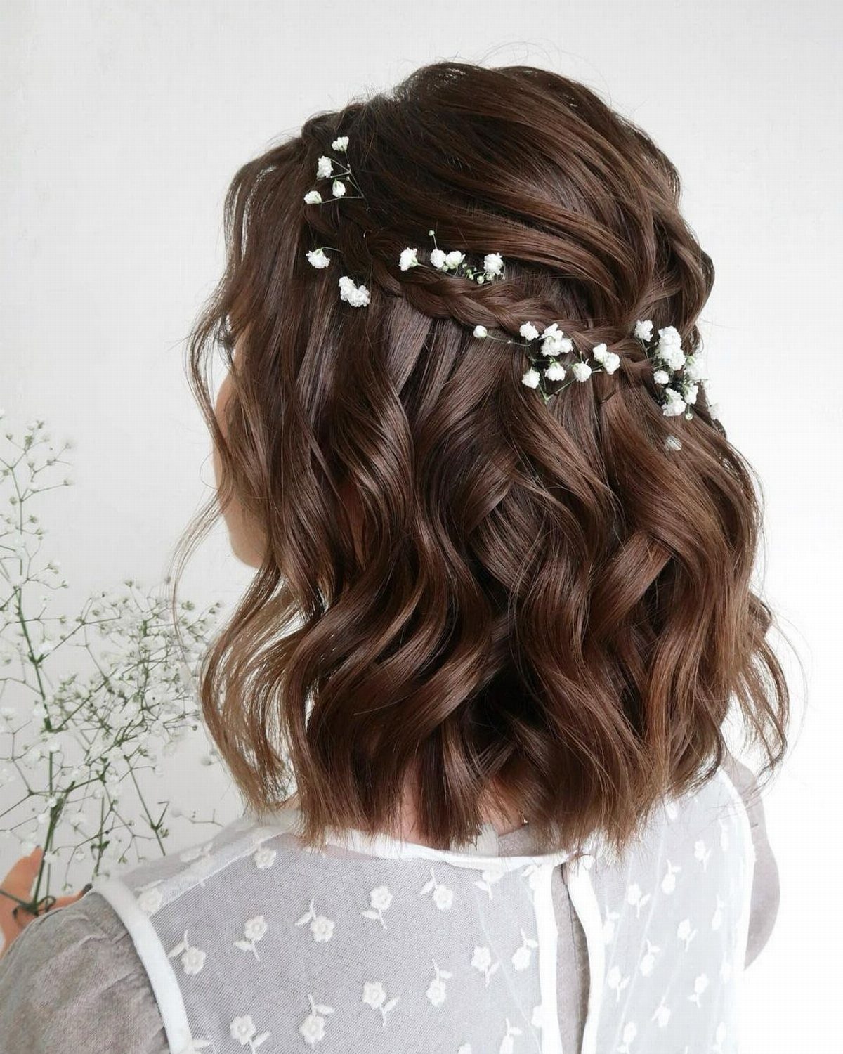 Shoulder-length wavy brown hair with small white flowers tucked into a loose braid.