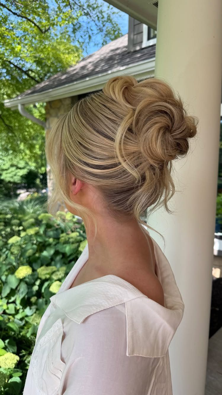 Blonde woman with a voluminous, textured updo and layered curls standing outdoors.