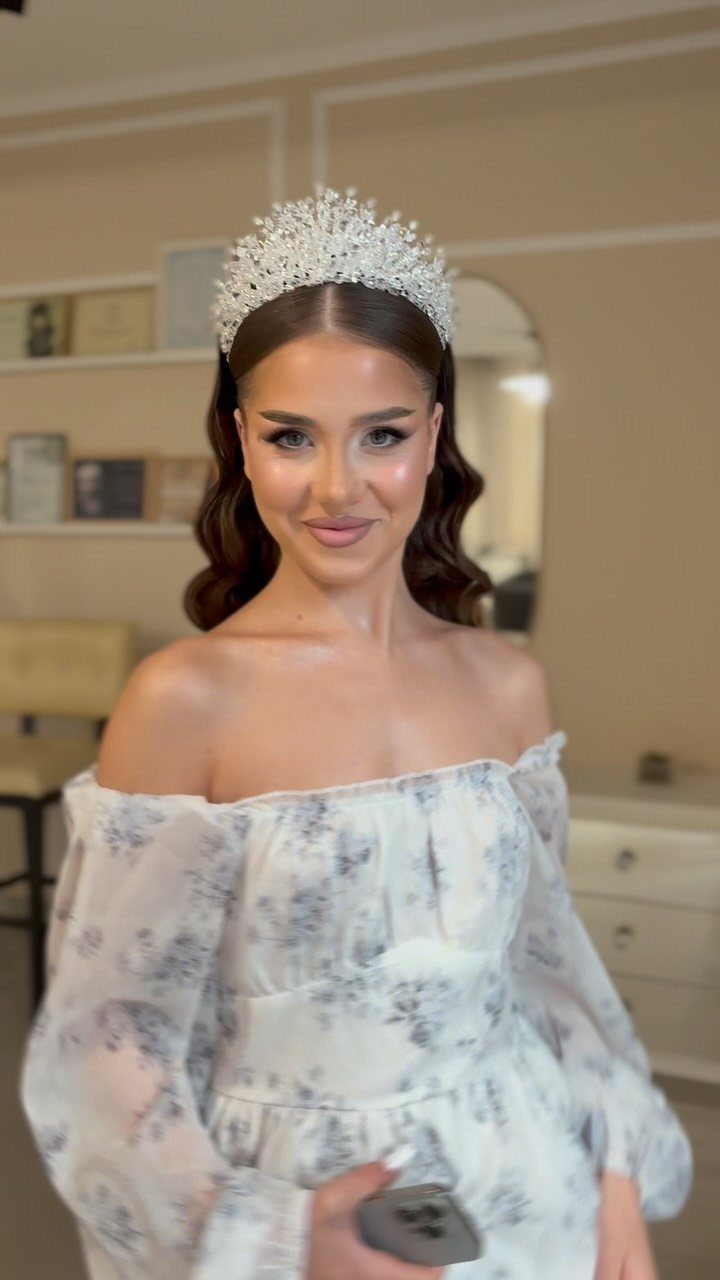 Woman with wavy brown hair wearing a sparkling silver tiara and white dress.