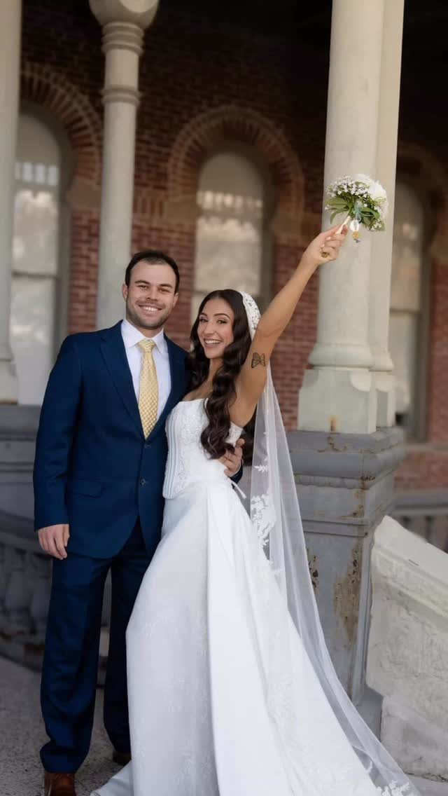Bride with long wavy hair and veil posing with groom in blue suit.