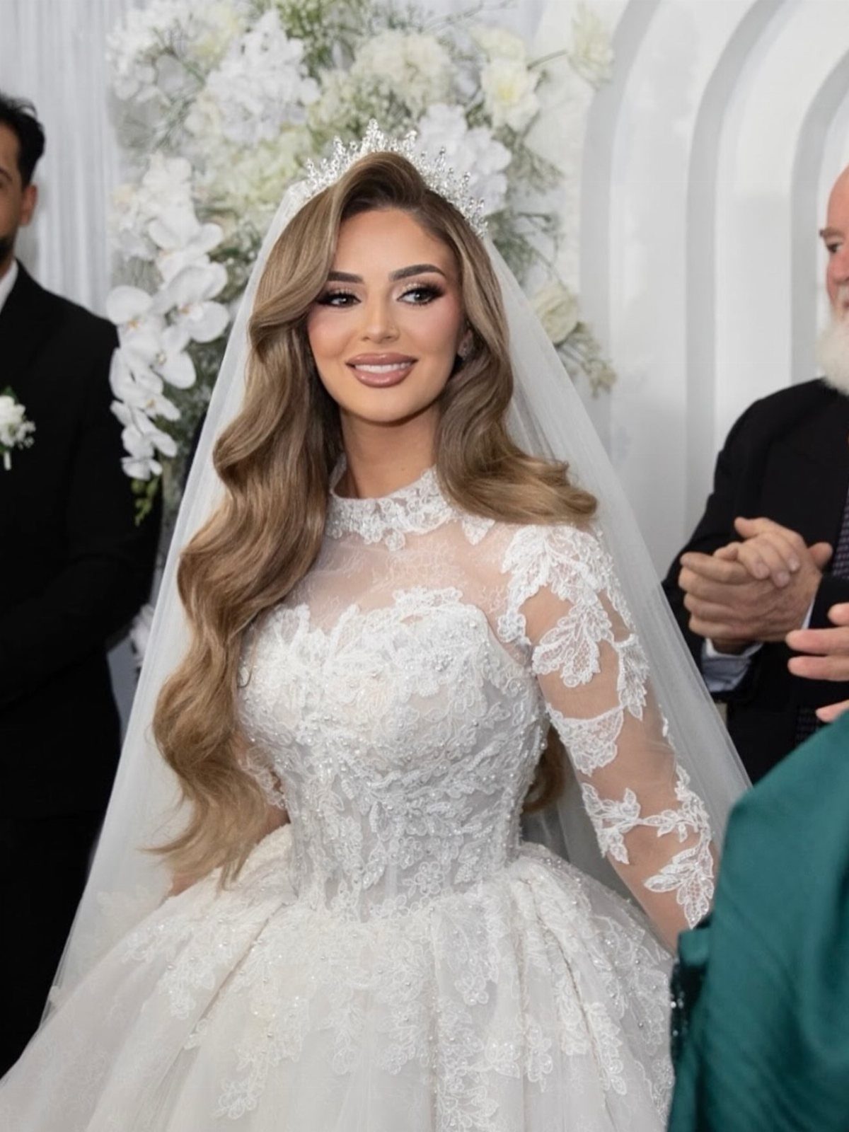 Woman with side-swept curls, a tiara, and a sheer white wedding veil.