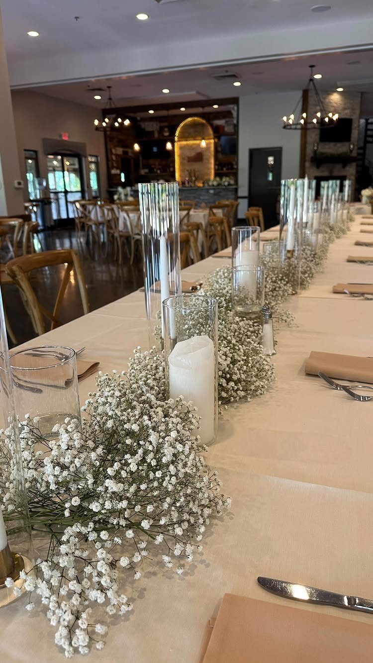 White baby's breath flowers and pillar candles in glass vases on a wedding table.