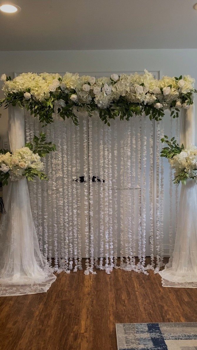 White fabric ceremony backdrop adorned with lush white flowers and green foliage.